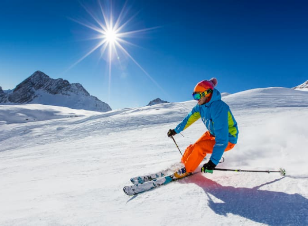 someone in full ski gear slides down a slope with the sun in the background