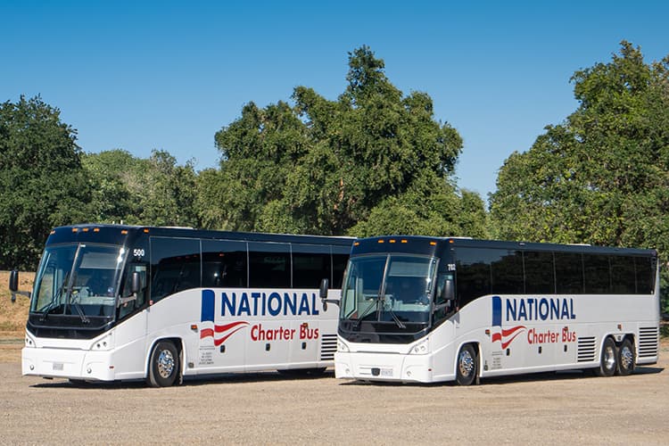 Two charter buses with National Charter Bus branding parked in a lot