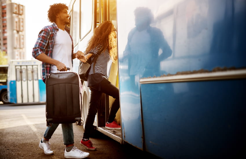 A young couple carries suitcases as they enter a bus