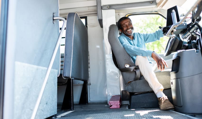 A bus driver smiles and sits in the driver seat of a charter bus