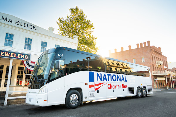 a large charter bus with the sun setting behind it