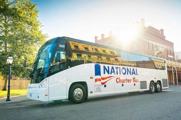 a large charter bus with the sun setting behind it