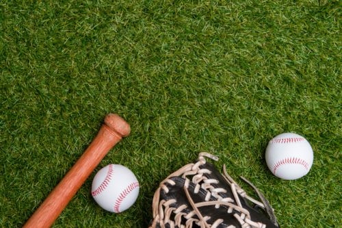 A baseball bat, glove, and two baseballs on a grassy field