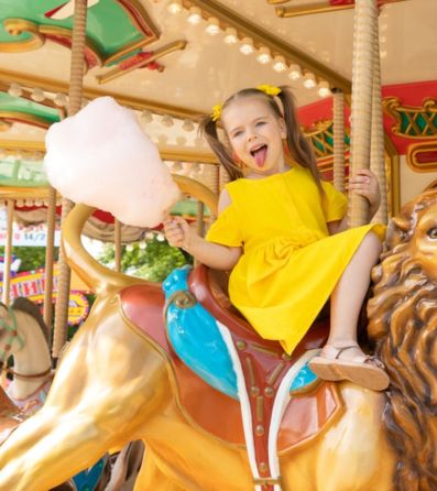 young girl holding cotton candy and riding a carousel