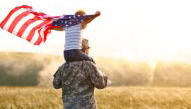 Soldier with a child on his shoulders while the child waves an American flag.