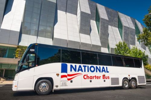 A National Charter Bus motorcoach parked outside a building with unique architecture